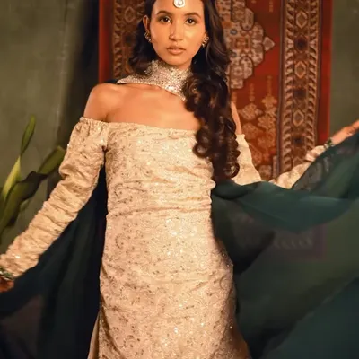 A full-length shot from a "Heeramandi" inspired photoshoot. I created a regal and vintage hairstyle with soft waves and a traditional maang tikka to complement the off-shoulder ethnic outfit.