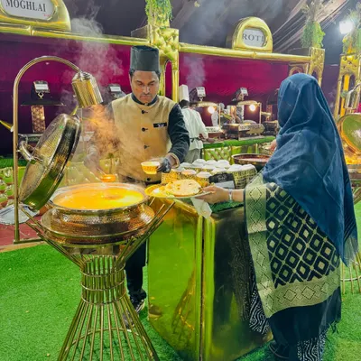 A guest is served a hot meal at my Mughlai food station. The setup features elegant golden chafing dishes and professional staff in traditional attire.