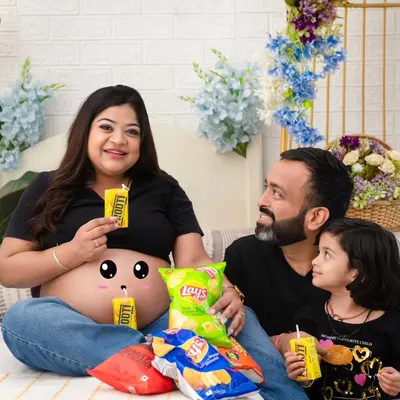 A fun and quirky family portrait celebrating pregnancy cravings. Sharing snacks and juice boxes, this family's playful energy is infectious. The cute drawing on the baby bump adds a whimsical touch.