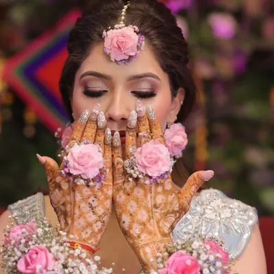 A beautiful shot capturing the essence of a Mehndi ceremony. The makeup features soft, shimmery eyes that complement the intricate henna and floral jewelry, creating a look that is both traditional and stunning.