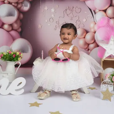 A playful shot from a first birthday milestone session. The birthday girl, dressed in a lovely white frock, shows off her personality with a pair of fun sunglasses, adding a touch of whimsy to her portraits.
