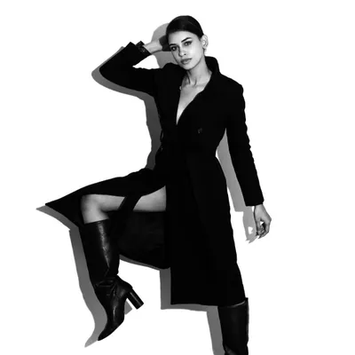 A dynamic full-length studio portrait in black and white. The high-contrast lighting and strong pose create a powerful fashion image that emphasizes the silhouette and attitude.