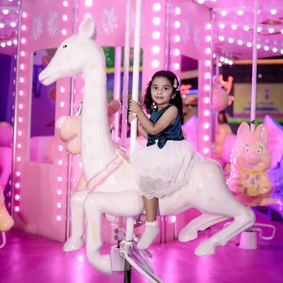 A magical moment from a child's birthday celebration, featuring a little girl riding a carousel horse. The bright pink lights of the merry-go-round create a whimsical and joyful atmosphere.