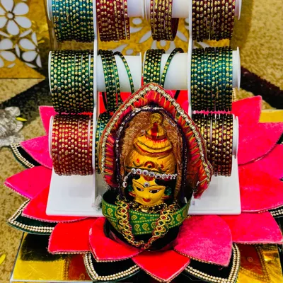 A beautiful bangle platter for a Gowri pooja or half-saree function. The goddess idol is placed in the center of a lotus-shaped base, surrounded by colorful glass bangles.