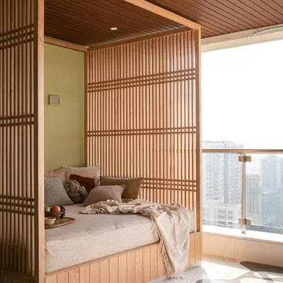 This cozy daybed, framed in wood and nestled in a high-rise balcony, creates the perfect spot for an afternoon siesta with a view of the Mumbai cityscape.