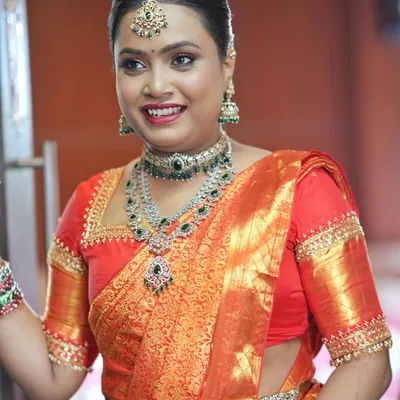 A radiant and happy bride at her engagement. This look features glowing skin, defined eyes, and a bright smile, perfectly matching her vibrant orange Kanjivaram saree and layered diamond jewellery.
