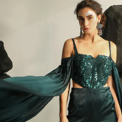 A breathtaking shot from an occasion wear campaign, capturing the dramatic flair of an emerald green embellished top with flowing sleeves. The styling and pose create a sense of movement and high drama.