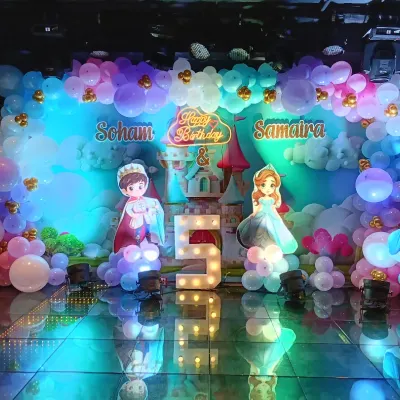 A full stage setup for a royal 5th birthday party. This Disney Princess theme features character cutouts, a castle backdrop, and a massive balloon arrangement in pastel colors, all illuminated with stage lighting for a dramatic effect.