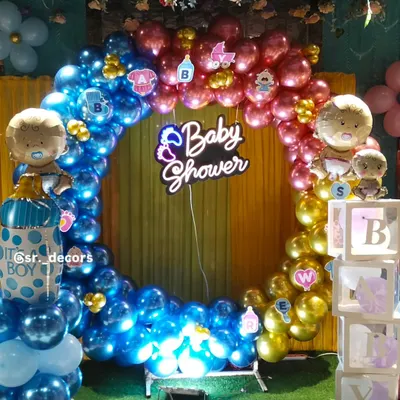 A full circular balloon arch in blue, pink, and gold creates a stunning photo booth for a baby shower. The glowing 'Baby Shower' neon sign in the center adds a modern and festive touch to the celebration.