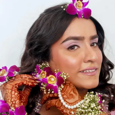 A close-up of a beautiful Haldi look. The makeup is subtle and elegant, with a soft lilac eyeshadow that picks up the color of the fresh orchids in her hair and jewellery.
