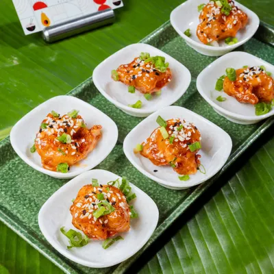 These are my Prawn Dynamite appetizers, served in individual portions. The crispy prawns are tossed in a creamy, spicy sauce and garnished with sesame seeds and spring onions, making them an instant party favorite.