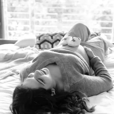 A quiet moment of bliss. This black and white lifestyle photo, with tiny baby shoes resting on the bump, captures the peaceful anticipation of waiting for your little one at home.