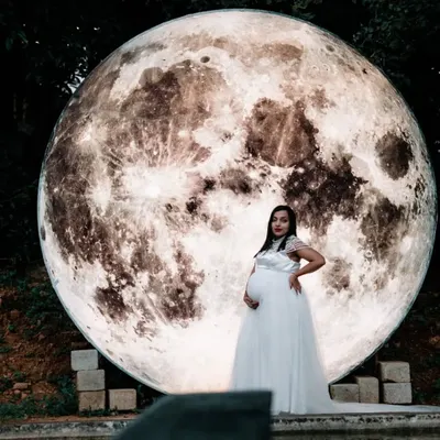 A breathtaking solo portrait of a mother-to-be in a white gown, standing before our giant illuminated moon prop. This is one of our signature creative concepts for an unforgettable night shoot.