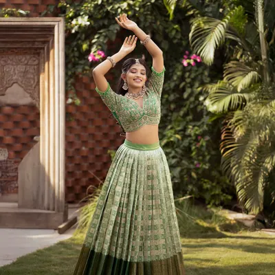 A joyful and vibrant Kanchi Pattu half saree in a refreshing pista green. The pleated lehenga creates a beautiful, full circle when twirling, and the look is completed with a heavily hand-embroidered crop top style blouse.