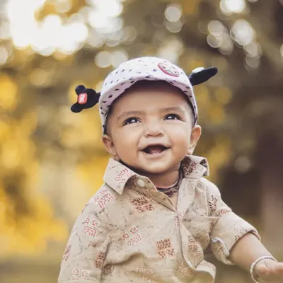 A beautiful outdoor portrait of a happy baby boy. The natural light and soft, leafy background create a warm and timeless feel, perfect for a child's portfolio.