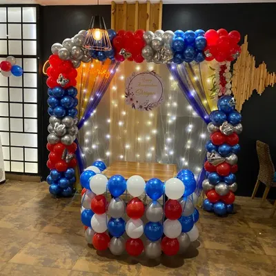 A bold Annaprashan ceremony decoration with a balloon pillar arch in red, blue, and silver. The setup includes a backdrop with fairy lights and a custom sign for the ceremony.