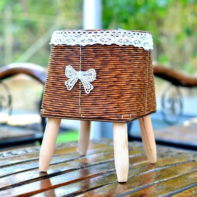 A chic, square-shaped woven planter on wooden tripod legs, perfect for a bohemian or rustic decor style.