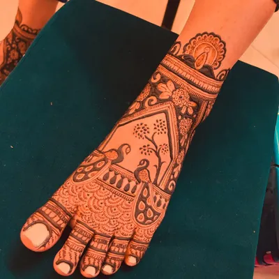 A full-coverage bridal foot mehendi design. This intricate pattern features peacock figures inside an architectural frame, covering the entire top of the foot.