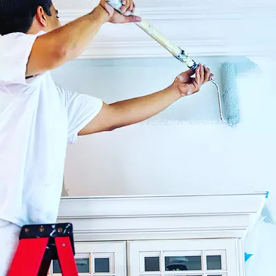 A painter using a roller with an extension pole to apply an even coat of paint near the ceiling. Using the right tools ensures a smooth, consistent finish without drips or marks.