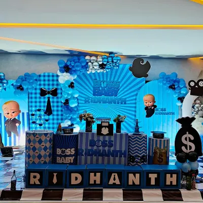 This "Boss Baby" theme for Ridhant is all about style and fun. The stage features a large backdrop with the movie's iconic sunburst design, character cutouts, and props like money bags and a director's clapperboard.