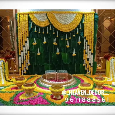 This is a complete setup for a homam or pooja ceremony. It features a traditional banana leaf backdrop, a vibrant floral rangoli on the floor, and brass urlis, creating a sacred and auspicious space.