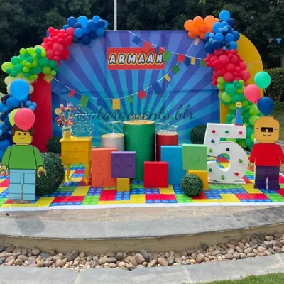 Welcome to a world of colorful bricks! This full stage setup for a 5th birthday features giant LEGO blocks, character cutouts, a light-up number, and a vibrant balloon arch.