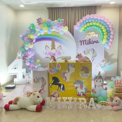 A complete unicorn and rainbow party setup with multiple unicorn props, a pastel rainbow balloon arch, and a large circular backdrop.