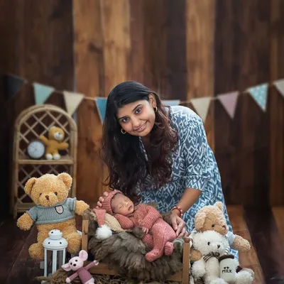 A mother's gentle touch. Here, a proud new mom poses with her sleeping baby, surrounded by adorable teddy bears in our cozy studio setup.