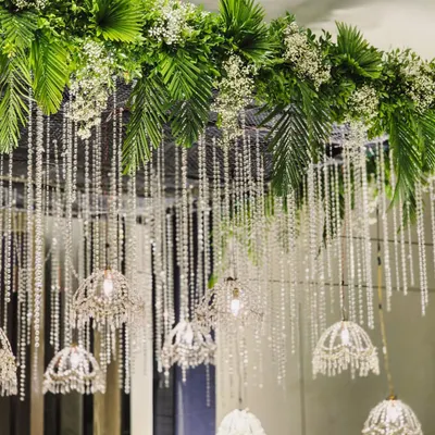 The canopy of a crystal entrance, showing how we blend lush greenery like palm fronds with delicate baby's breath and sparkling crystal strings for a look of modern opulence.