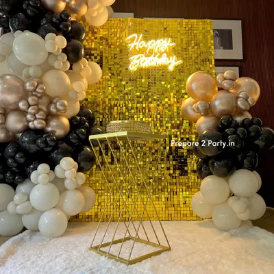 A sophisticated birthday setup featuring a gold sequin wall and a neon sign. The look is completed with an elegant balloon garland in black, white, and champagne gold, and a modern cake stand.