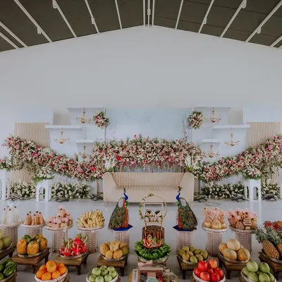 A wide shot showcasing the breathtaking decor of a naming ceremony. The stage is adorned with cascading flowers and traditional fruit offerings, setting a beautiful scene for the day's events.