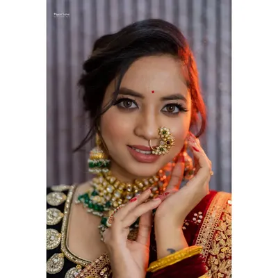 A stunning close-up bridal portrait. The focus is on the bride's flawless makeup, intricate nose ring (nath), and sparkling eyes, capturing the beauty and excitement of her special day.