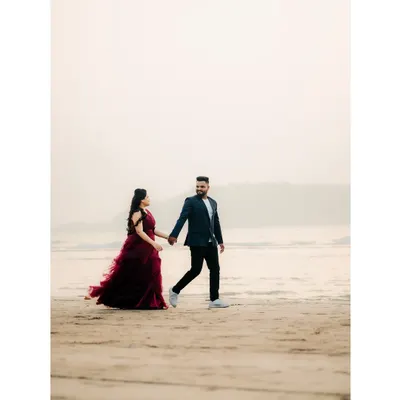 A classic pre-wedding photo of a couple walking hand-in-hand on the sand, with the bride's gown flowing beautifully.