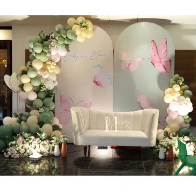 A 'Baby in Bloom' baby shower with a beautiful butterfly theme. The setup includes custom arched backdrops, a comfortable sofa for the mom-to-be, and an elegant organic balloon garland in sage green and pastel pink.