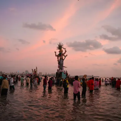 The Mumbaicha Raja idol during Visarjan, silhouetted against a breathtaking pink sunset. This photo captures the immense scale of the festival and the collective emotion of the farewell.