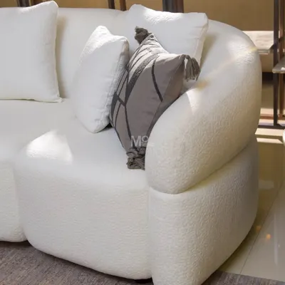 A close-up of the Aether Sofa's gracefully curved arm, showcasing the soft, looped texture of the high-quality bouclé fabric that invites you to sink in and unwind.
