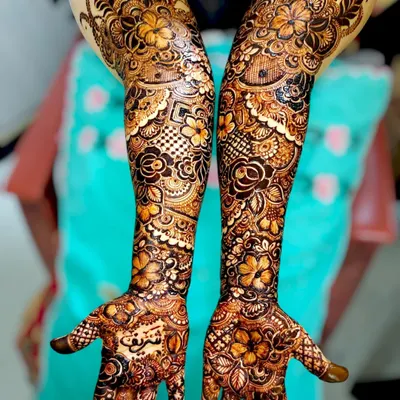 A complete bridal henna set, showcasing how the intricate patterns flow from the palm to the forearm. This design mixes floral elements with traditional Indian mehndi patterns.
