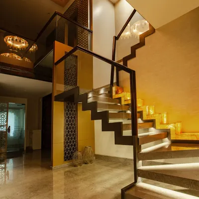 A modern floating staircase with stone treads and ambient under-step lighting, framed by sleek glass and wood railings. The classic trellis pattern in the backdrop adds a timeless touch to this contemporary design.
