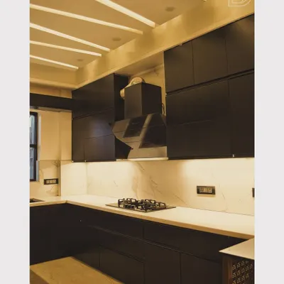 A sleek, modern kitchen from one of our completed projects. It features dark, handleless cabinets, a white marble backsplash, and a powerful chimney, all illuminated by stylish ceiling beams with integrated lights.