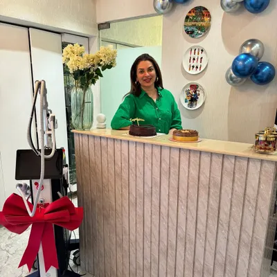 Standing at the reception desk of my clinic. We recently added a new machine to our practice, and I'm excited to offer the latest technology to help you level up your skincare game.