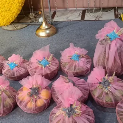 Beautifully wrapped return gifts for a baby shower. These small baskets of fruits are covered in pink netting with a blue flower on top, making them a lovely and thoughtful favor for your guests.