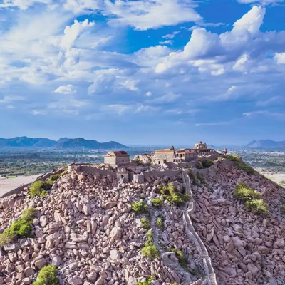 A breathtaking aerial view of the historic Gingee Fort in Tamil Nadu, capturing the ancient structure perched atop a rocky hill under a dramatic sky.