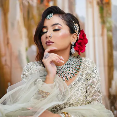 A beautiful modern glam look featuring golden cut-crease eyeshadow, a bold red flower in the hair, and a stunning diamond and emerald necklace.