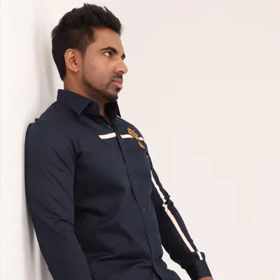 This navy blue shirt features a clean white stripe that runs across the chest and down the sleeve, accented by a small, intricate golden crest. It's a design that balances modern lines with classic, regal details.