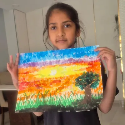 A young student, Krishika, proudly displays her sunset landscape created using a finger painting technique. This method is a fun, tactile way for children to learn about color blending.