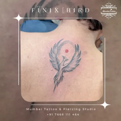 A phoenix rising, tattooed on the back. This symbol of rebirth and new beginnings is rendered with soft grey shading to give the wings a sense of light and movement.