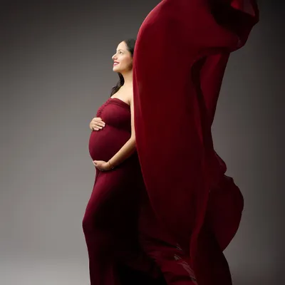 Capturing the beauty of movement, this shot features a vibrant red gown with a flowing train against a classic grey backdrop. This technique adds a dynamic and artistic flair to the maternity portrait.