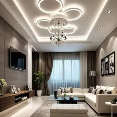 This living room features a complex and modern false ceiling design with a unique circular LED fixture combined with a chandelier. The multi-layered lighting creates a bright yet comfortable environment.