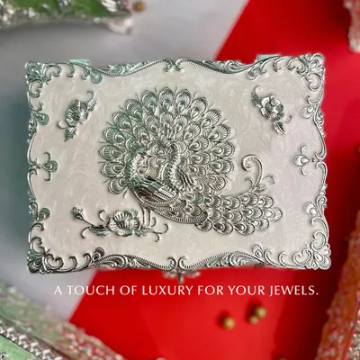 A touch of luxury for your jewels. This white enamel box features a stunning silver peacock, its feathers unfurled in a display of regal beauty. It is a perfect piece for your dressing table.