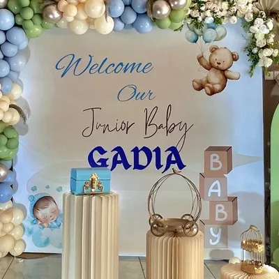 A 'Welcome Baby Boy' setup for the Gadia family. This design features a personalized backdrop, a gentle color palette of sage green, blue, and beige balloons, and cute teddy bear accents.